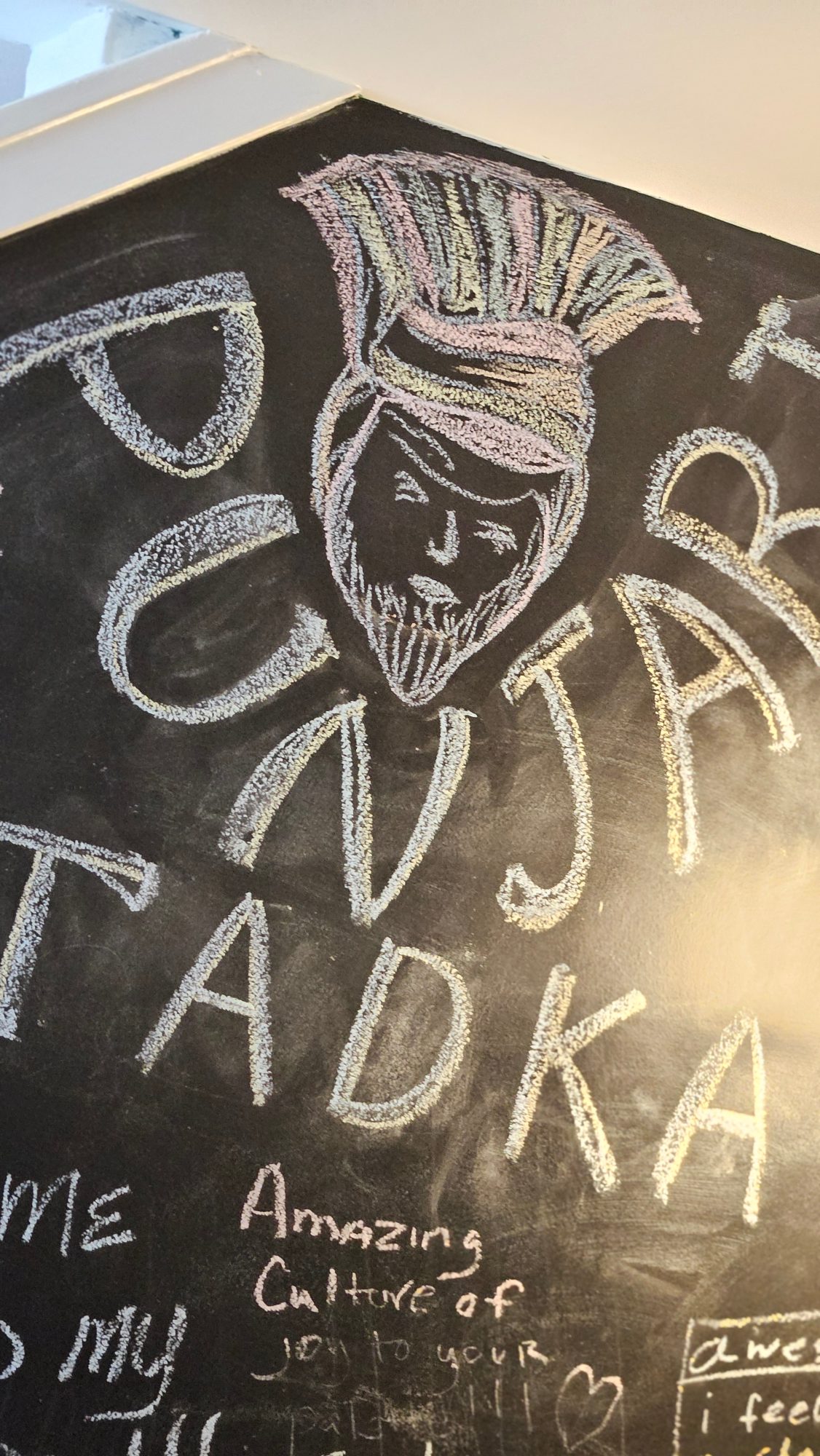 Guests writing notes in chalk on the Punjabi Tadka chalkboard wall
